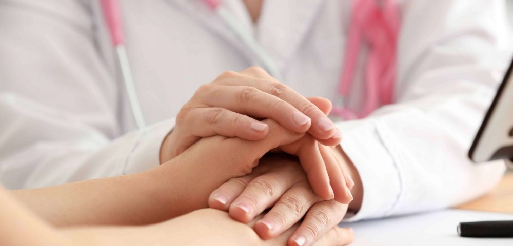A doctor wearing a pink ribbon and holding the hands of a patient.